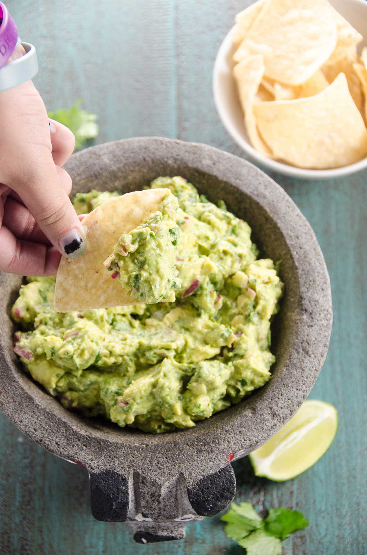 4 ingredient guacamole recipe in a molcajete with a child's hand dipping a tortilla chip