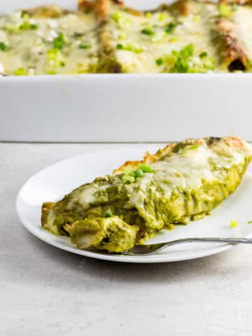 chicken and black bean enchiladas with green enchilada sauce in a pan and on a plate with a fork