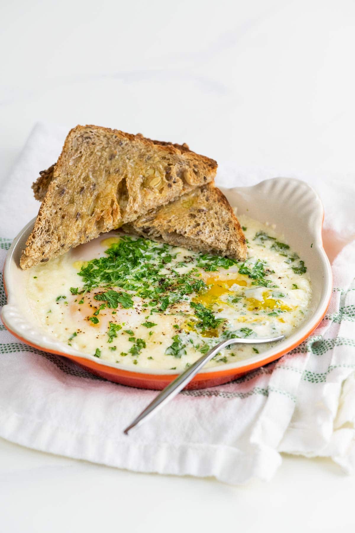 oeufs en cocotte (french baked eggs) with toast and a fork on a cloth napkin