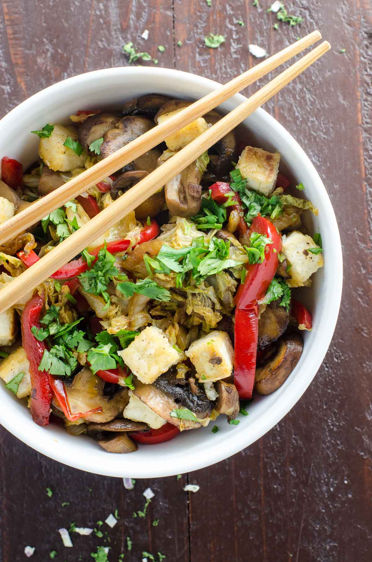 napa cabbage stir fry with salt and pepper tofu, mushrooms, and red bell pepper in a bowl with chopsticks