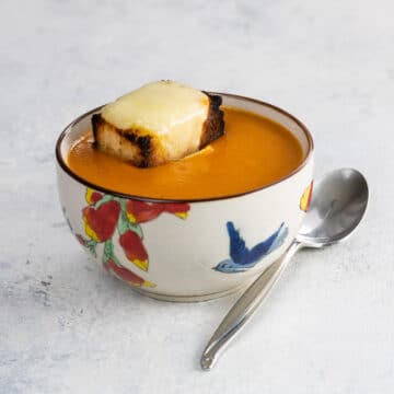 a bowl of old fashioned tomato soup with grilled cheese crouton and spoon