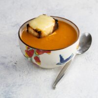 a bowl of old fashioned tomato soup with grilled cheese crouton and spoon