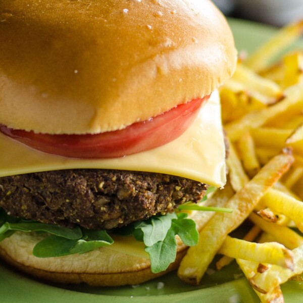 a vegan lentil burger on a bun with cheese, tomato, and lettuce, and baked yukon gold french fries on a plate with ketchup