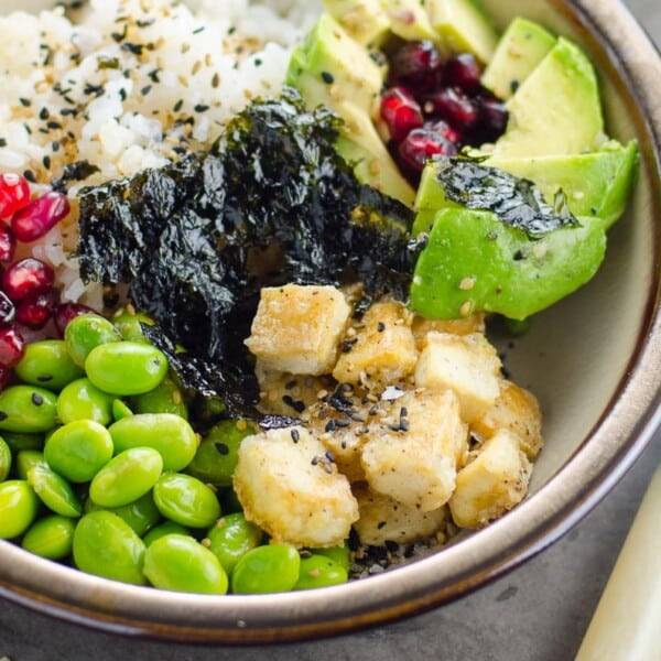 a vegan sushi bowl with salt and pepper tofu, edamame, sushi rice, nori, avocado, pomegranate arils, and citrus vinaigrette