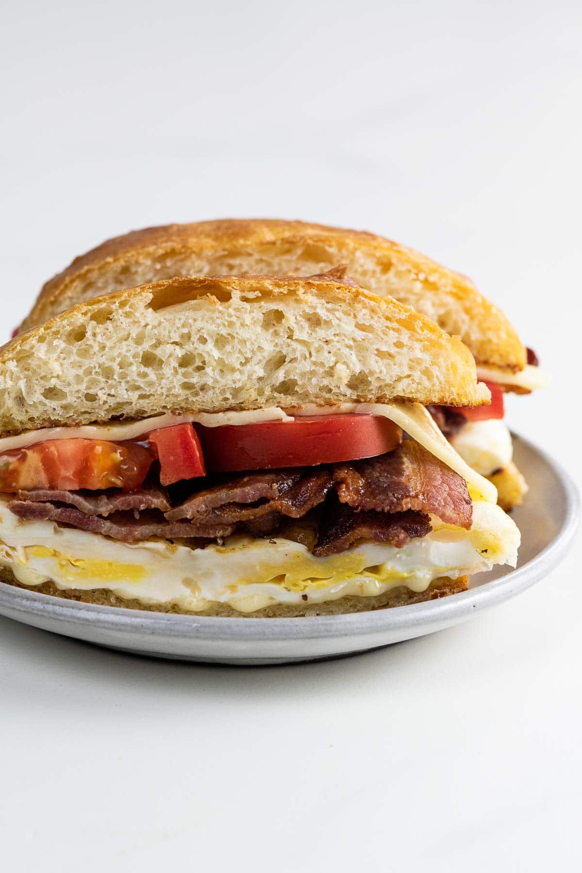 a bacon egg and cheese sandwich with tomato on a potato bun