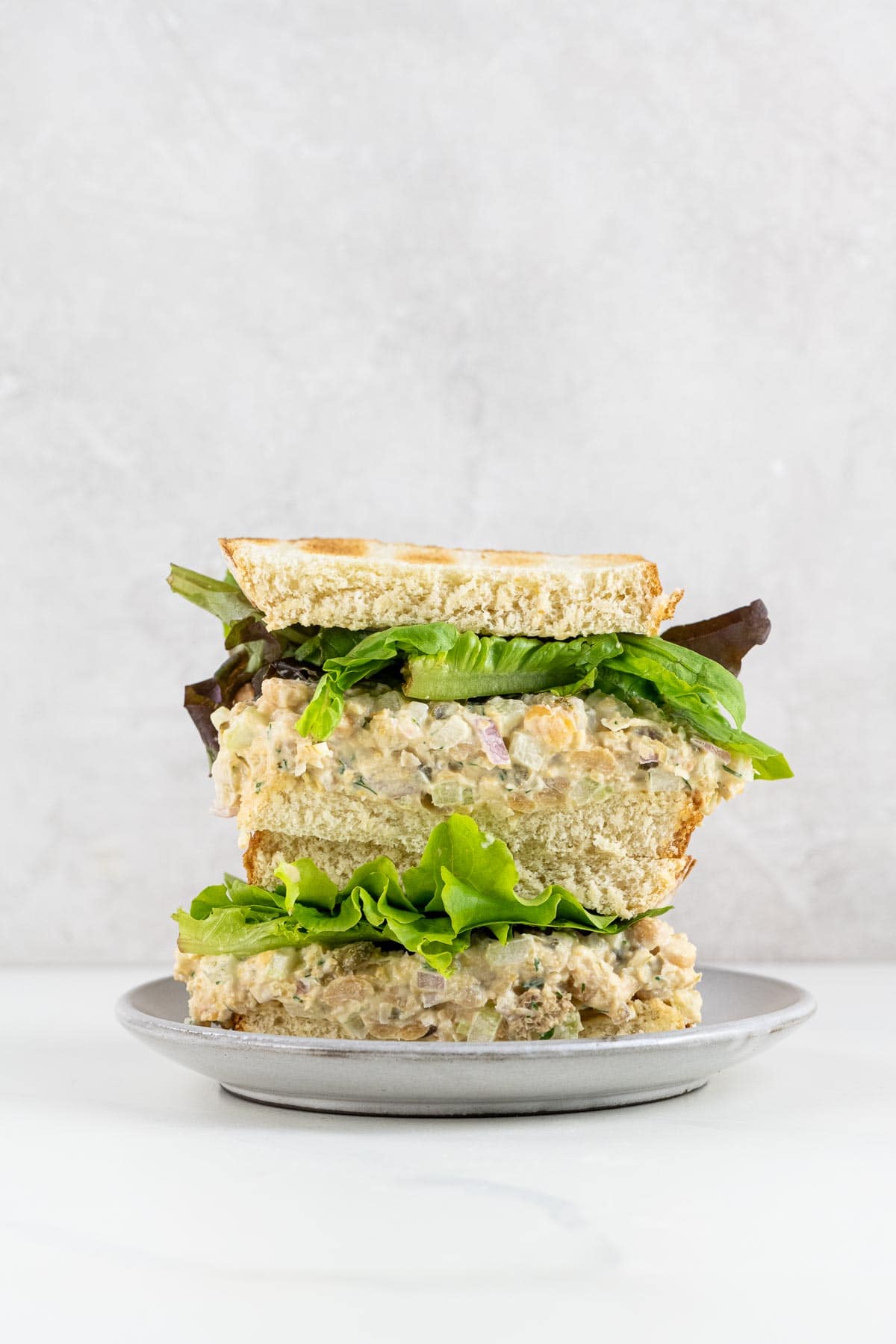 a chickpea tuna salad sandwich on toasted white bread with mixed greens