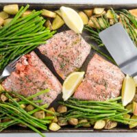 salmon, potatoes, and asparagus on a sheet pan with a fork, a spatula, and lemon wedges