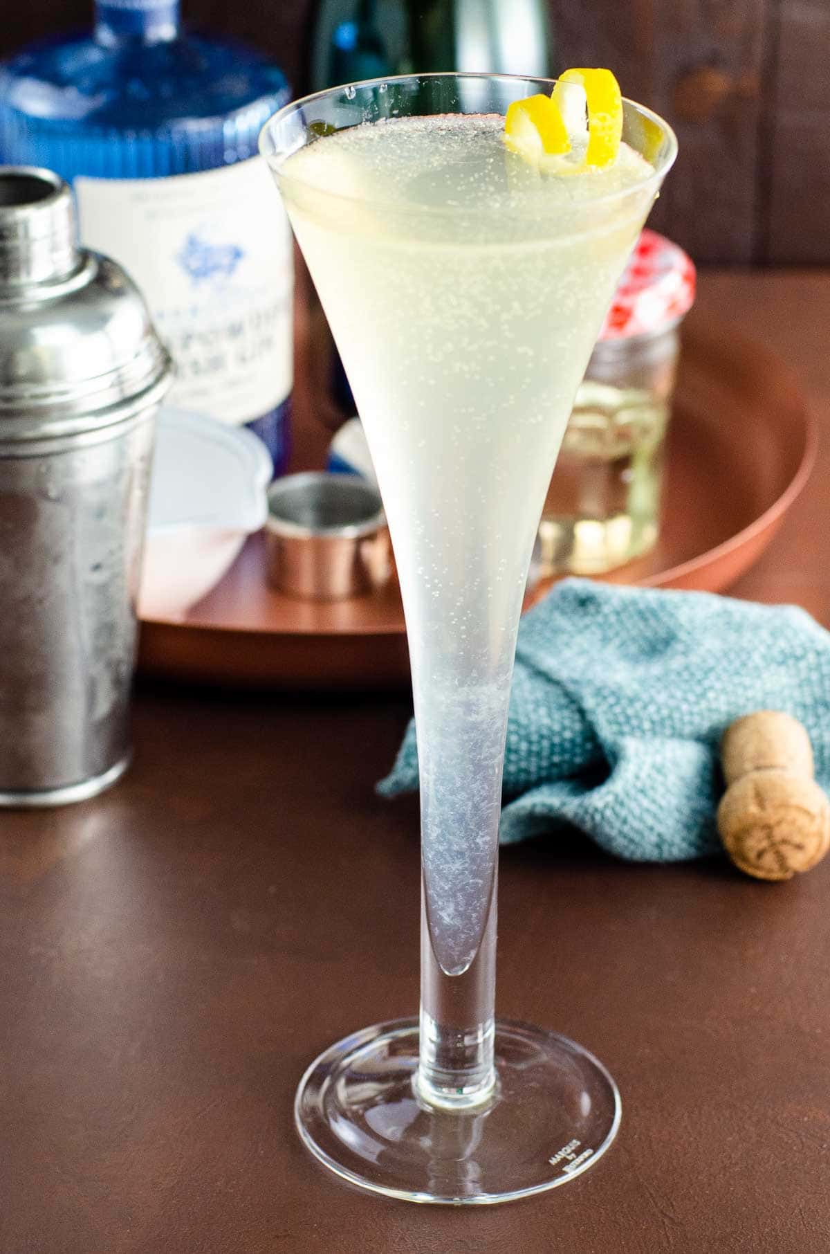 a soixante quinze gin champagne cocktail (french 75) in a glass with a lemon twist on a table with ingredients behind it