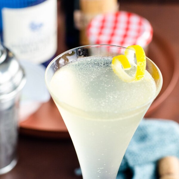 a soixante quinze gin champagne cocktail (french 75) in a glass with a lemon twist on a table with ingredients behind it