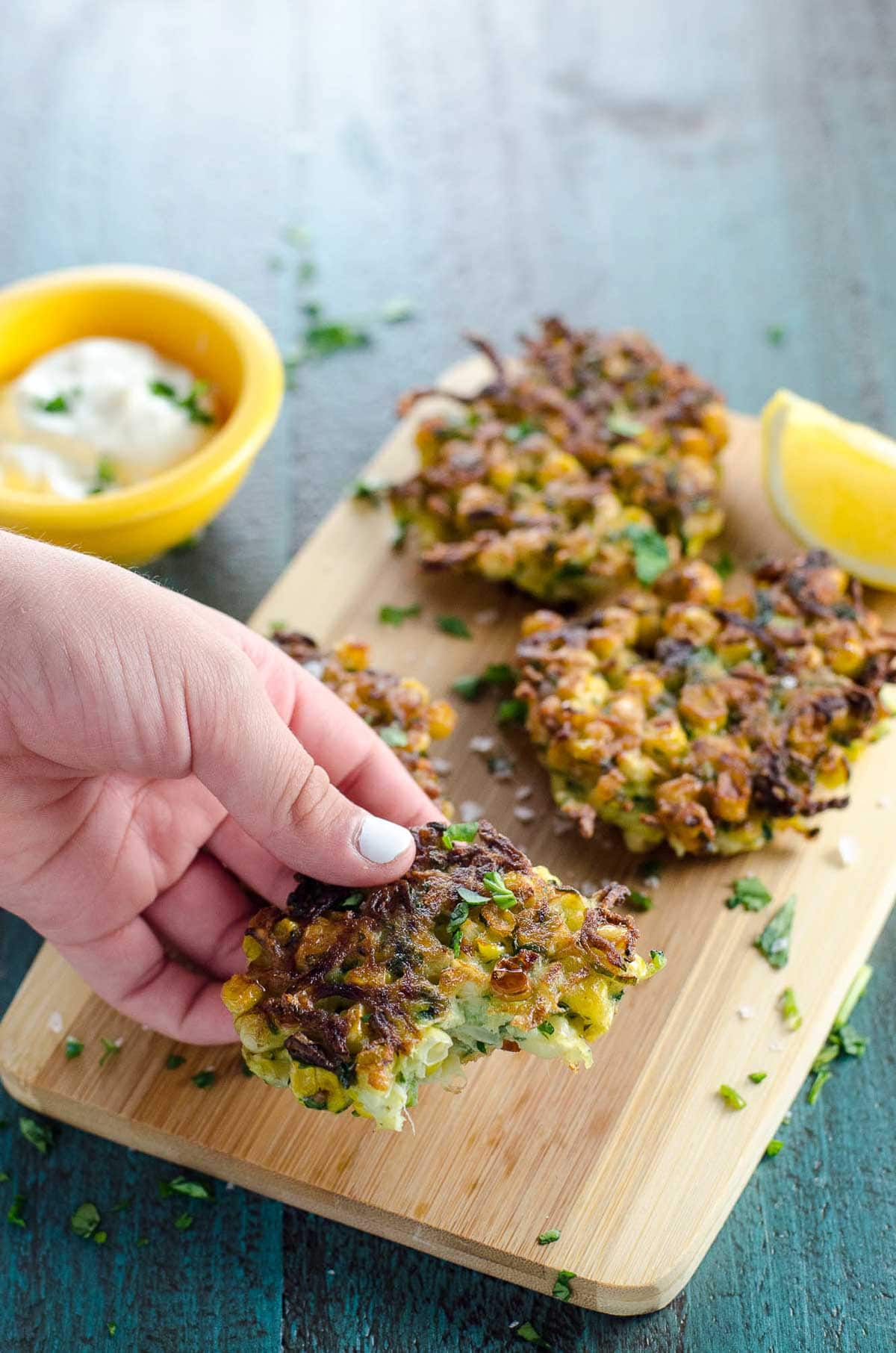 a child's hand picking up a zucchini and corn fritter