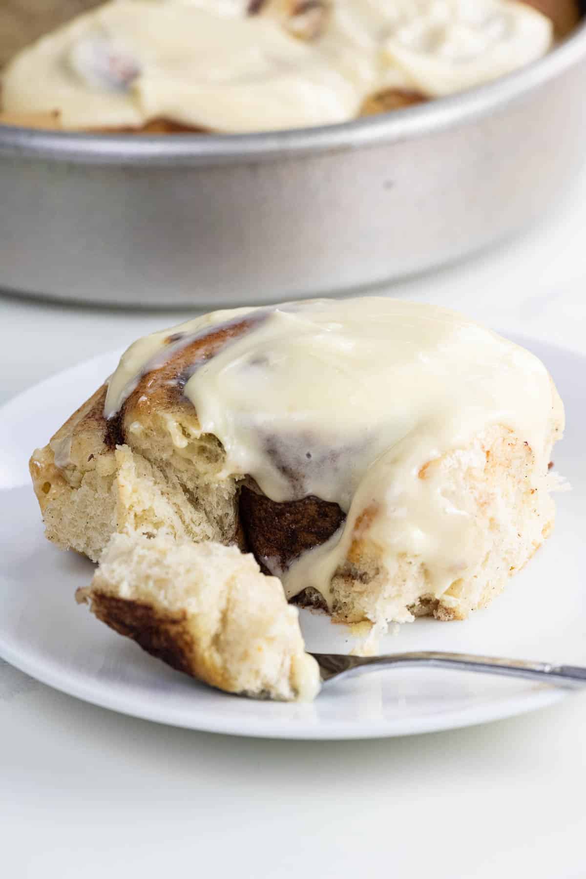 a brioche cinnamon roll with cream cheese icing on a plate with a fork