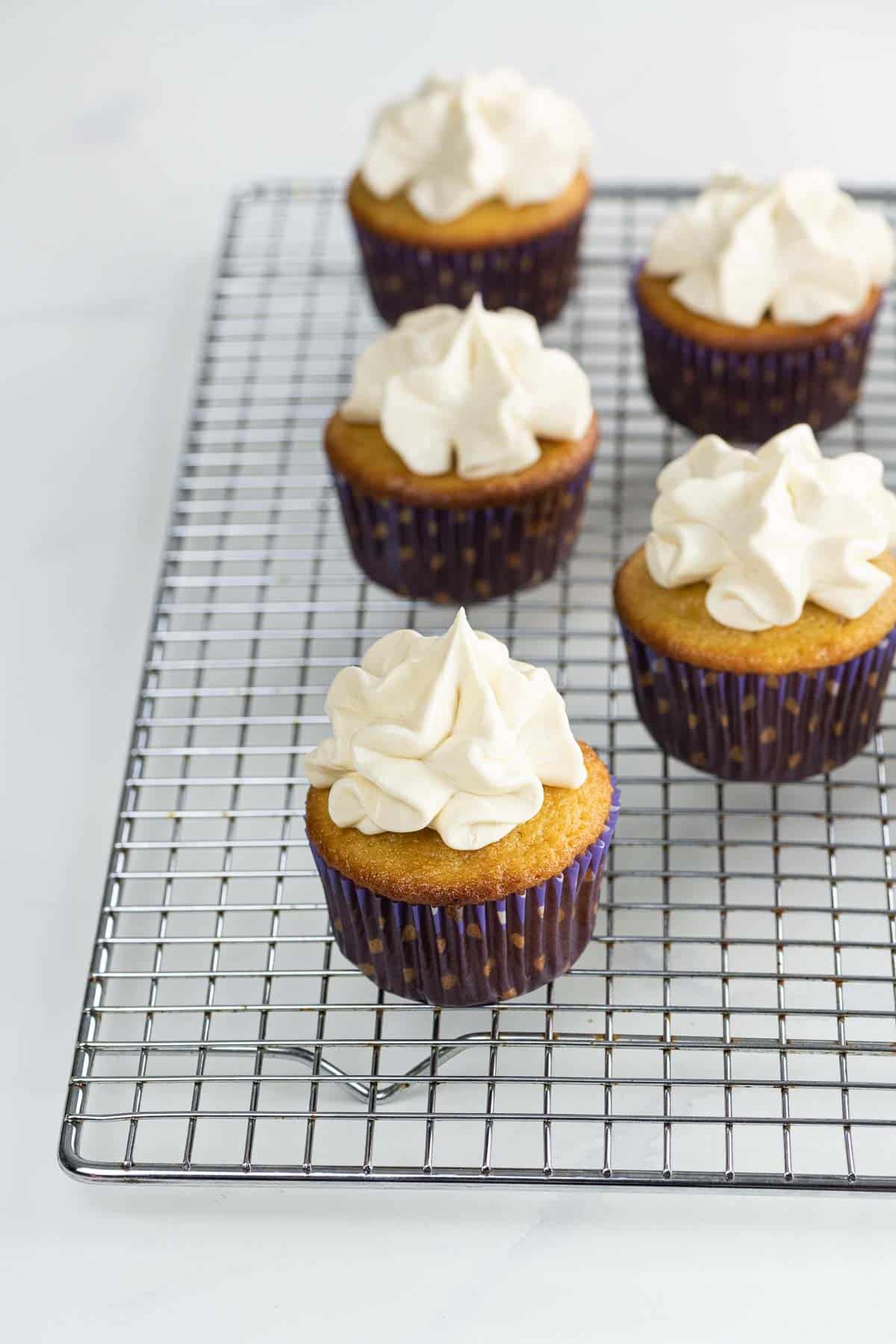 ultimate vanilla cupcakes with whipped buttercream frosting on a cooling rack