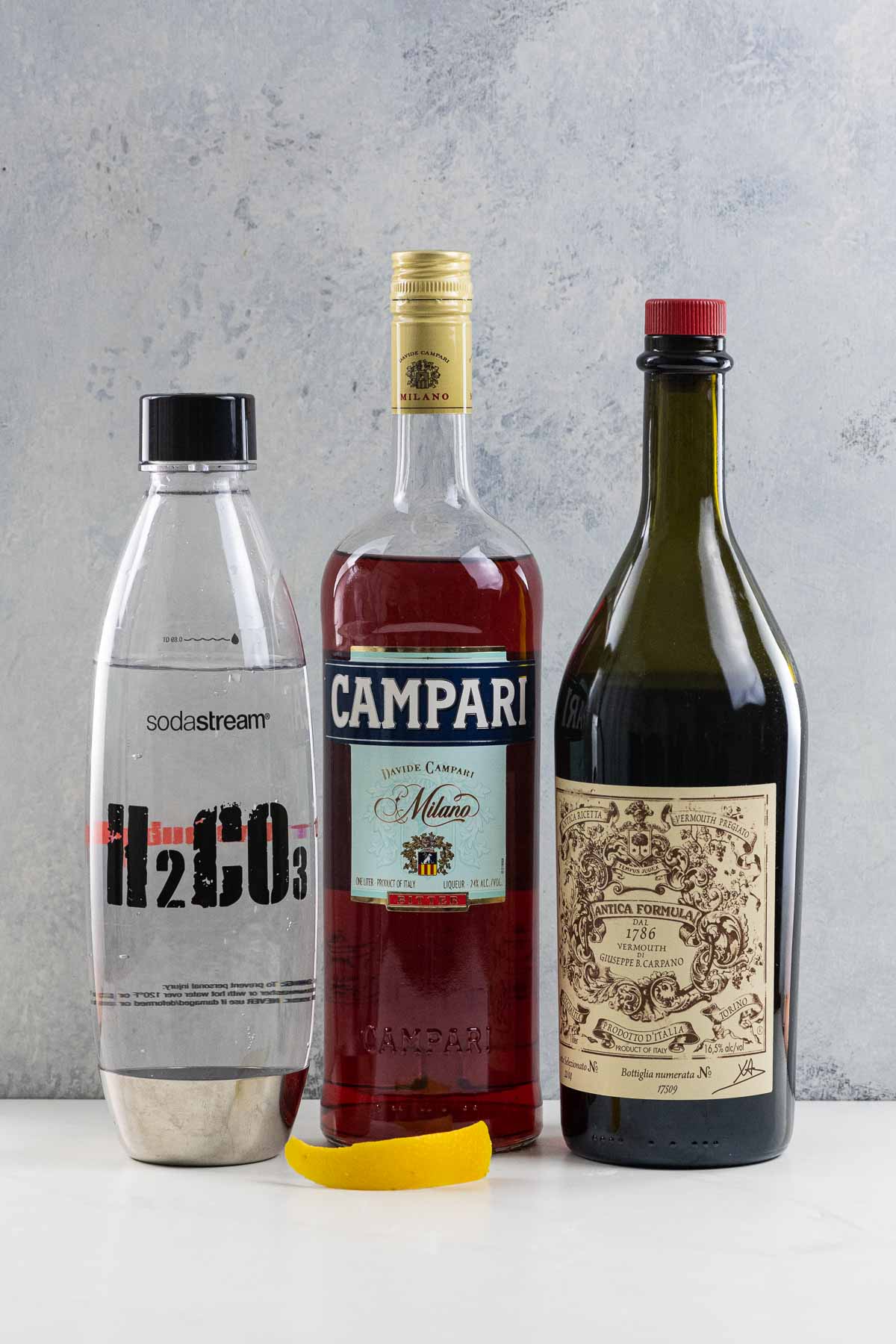 ingredients for an Americano cocktail (campari, carpano antica sweet vermouth, soda water, and an orange twist)