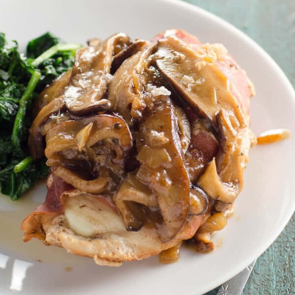 prosciutto wrapped stuffed chicken marsala on a plate with sauteed spinach