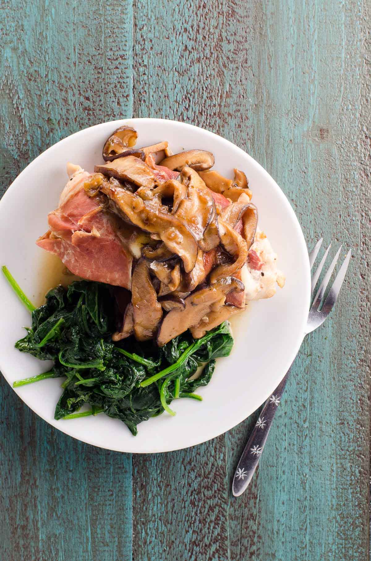 prosciutto wrapped stuffed chicken marsala on a plate with sauteed spinach