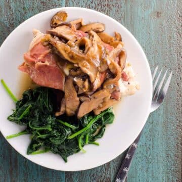 prosciutto wrapped stuffed chicken marsala on a plate with sauteed spinach