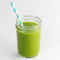 a banana spinach smoothie in a mason jar with a striped paper straw