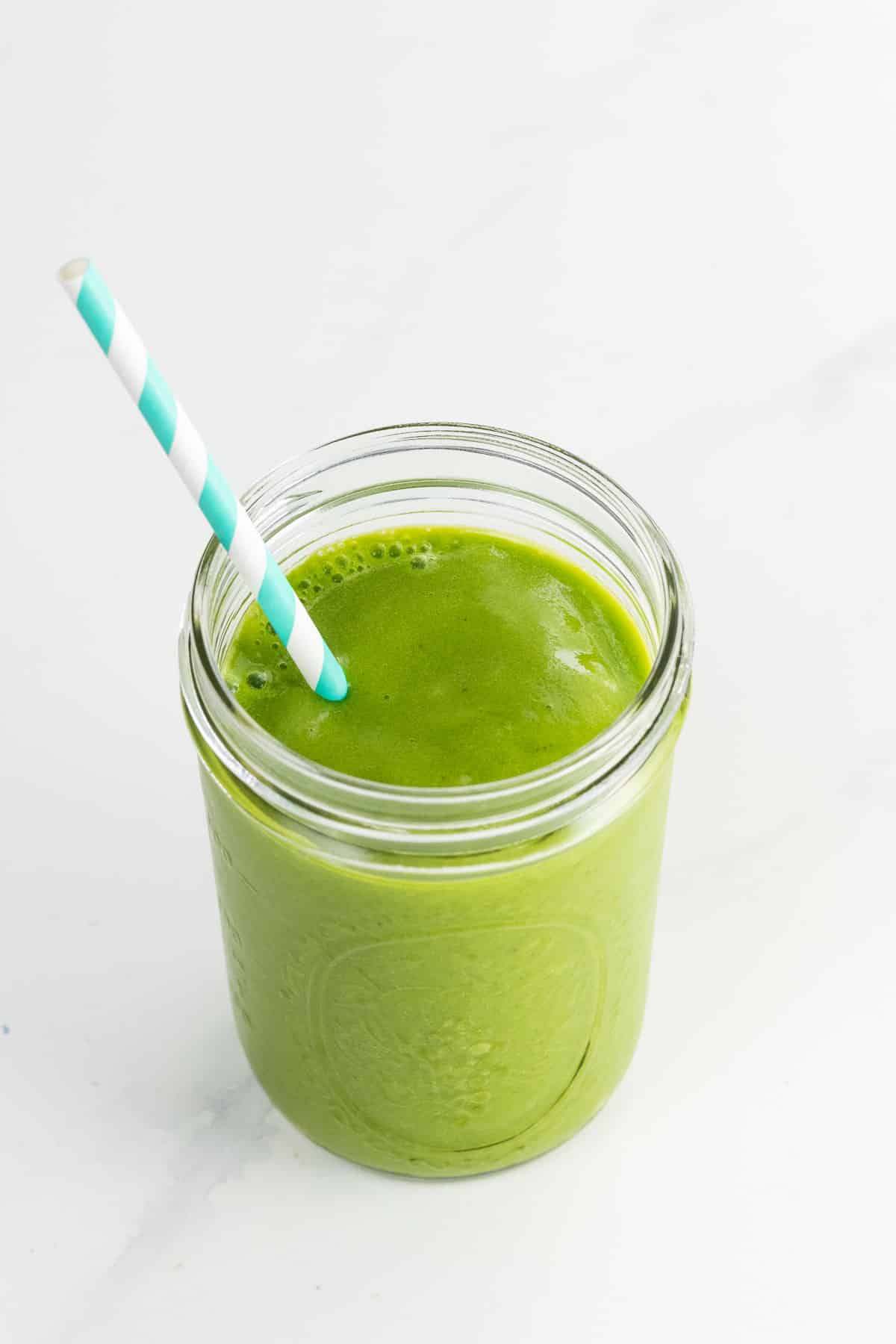 a banana spinach smoothie in a mason jar with a striped paper straw