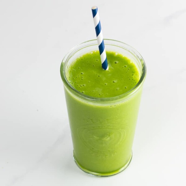 a pineapple spinach smoothie in a glass with a straw