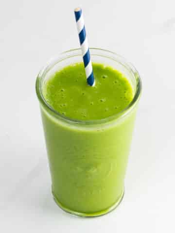 a pineapple spinach smoothie in a glass with a straw