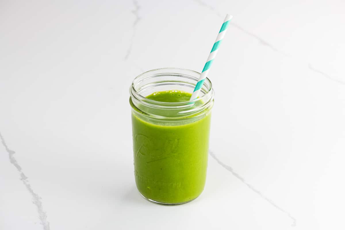 a mango spinach smoothie in a mason jar with a striped paper straw