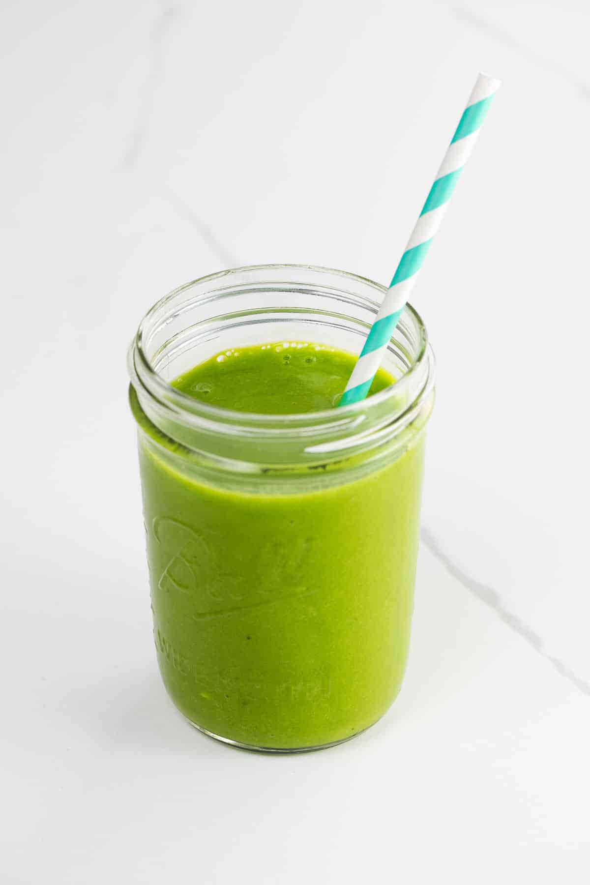 a mango spinach smoothie in a mason jar with a striped paper straw