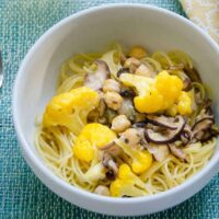 umami pasta with cauliflower, shiitakes, and chickpeas in a bowl with a glass of white wine