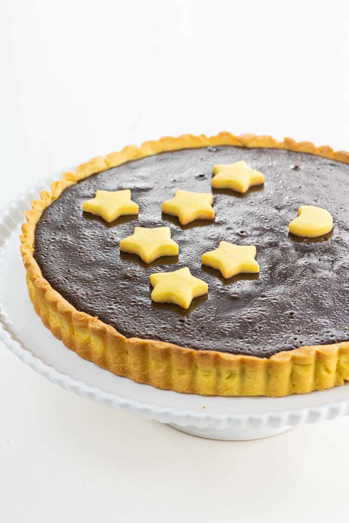 a bittersweet chocolate ganache tart with shortbread crust on a cake stand