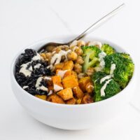 a black rice bowl with maple roasted butternut squash, sauteed chickpeas, broccoli, and tahini dressing