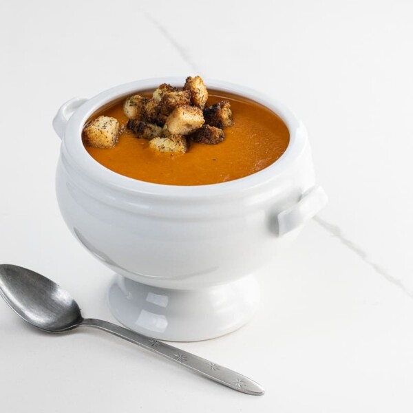 creamy vegan tomato soup with croutons in a footed bowl with a spoon