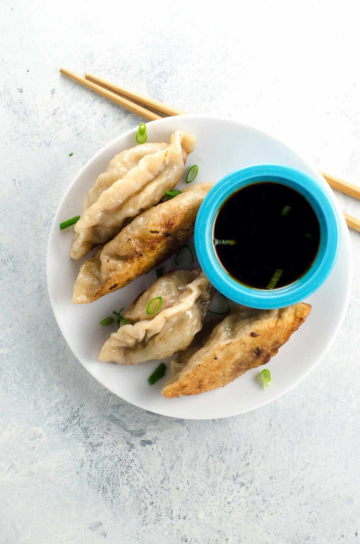 pork dumplings on a plate with dipping sauce and chopsticks