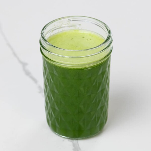 spinach juice with pineapple, green apple, and lime in a small glass