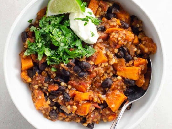 Instant Pot sweet potato chili with black beans, buckwheat, and chipotle in a white bowl garnished with lime, sour cream, and cilantro