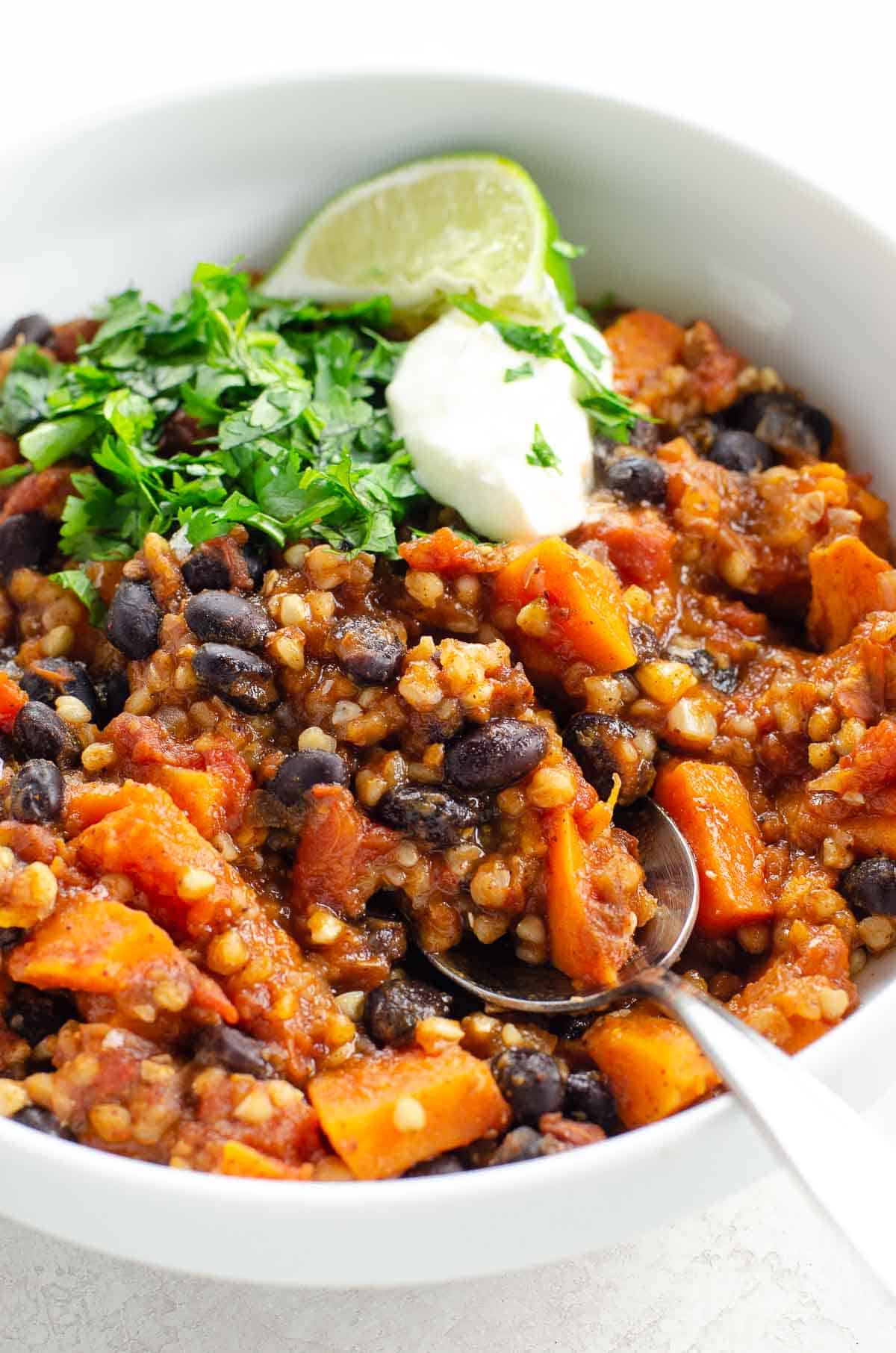 Instant Pot sweet potato chili with black beans, buckwheat, and chipotle in a white bowl garnished with lime, sour cream, and cilantro