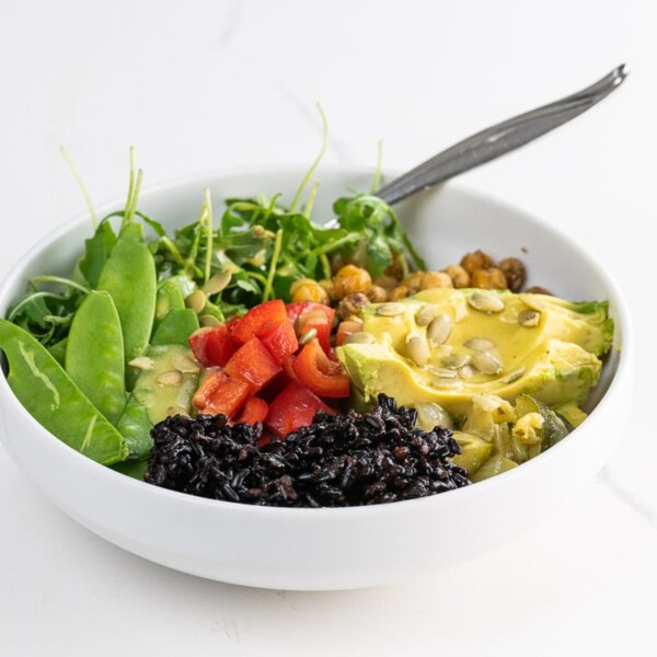 a vegan buddha bowl with forbidden rice, avocado, sauteed chickpeas, snow peas, red bell pepper, arugula, creamy lemon vinaigrette, and pepitas