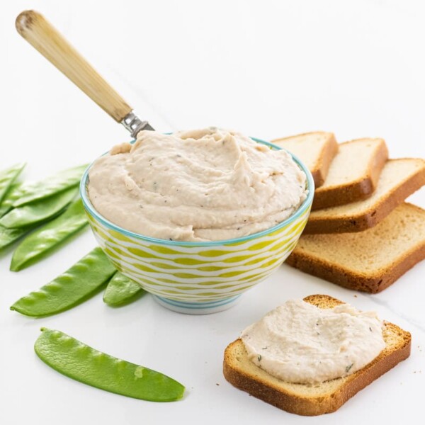 white bean dip in a decorative bowl with snow peas and brioche toasts