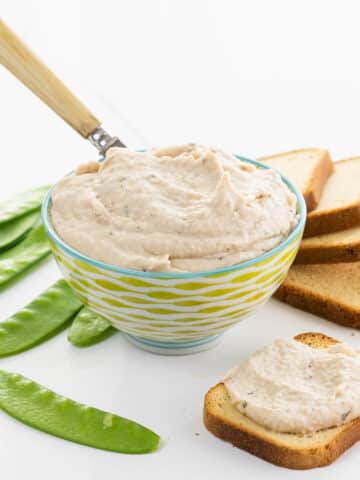 white bean dip in a decorative bowl with snow peas and brioche toasts