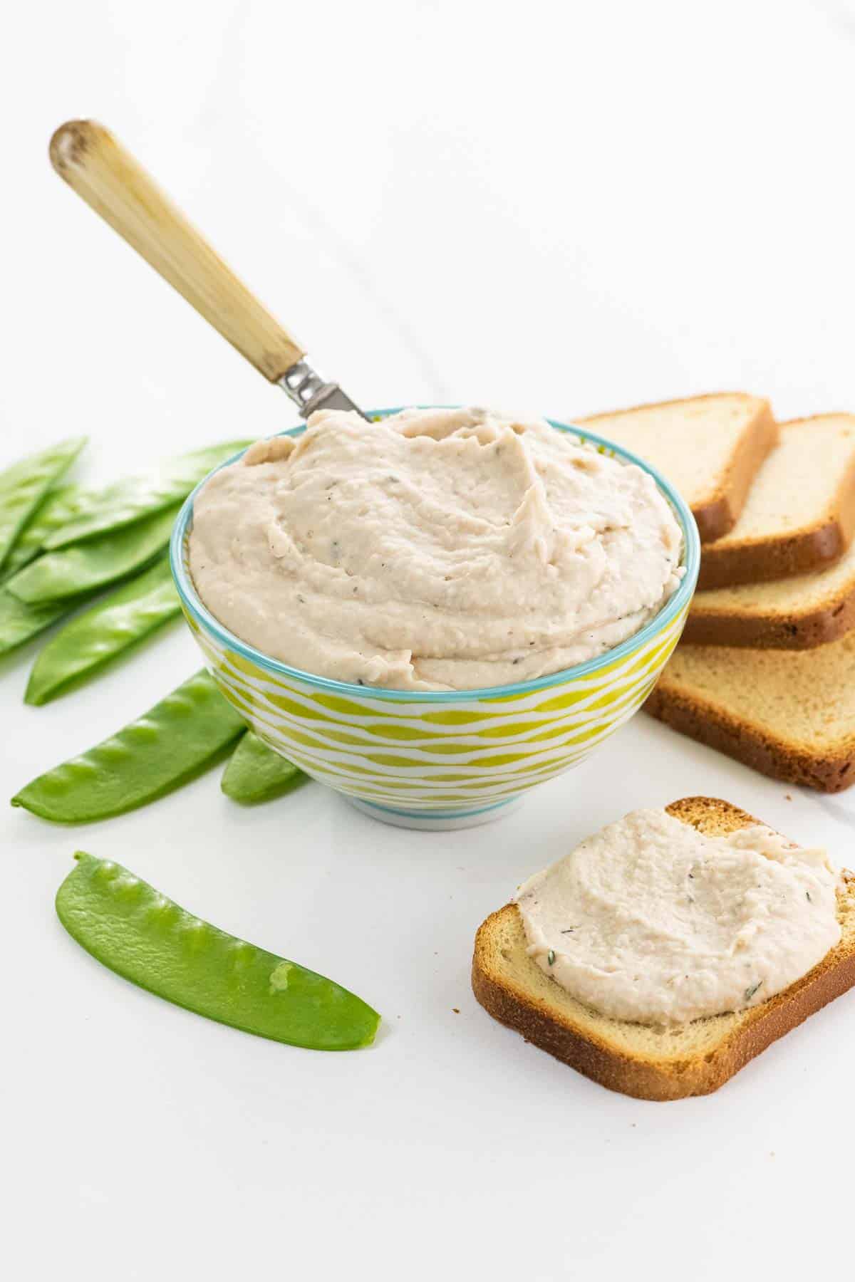 white bean dip in a decorative bowl with snow peas and brioche toasts