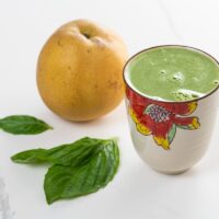 asian pear juice with basil, lemon, and celery in a decorative glass with basil leaves and an asian pear