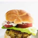a crab cake sandwich on a kaiser roll with lettuce, tomato, and tartar sauce