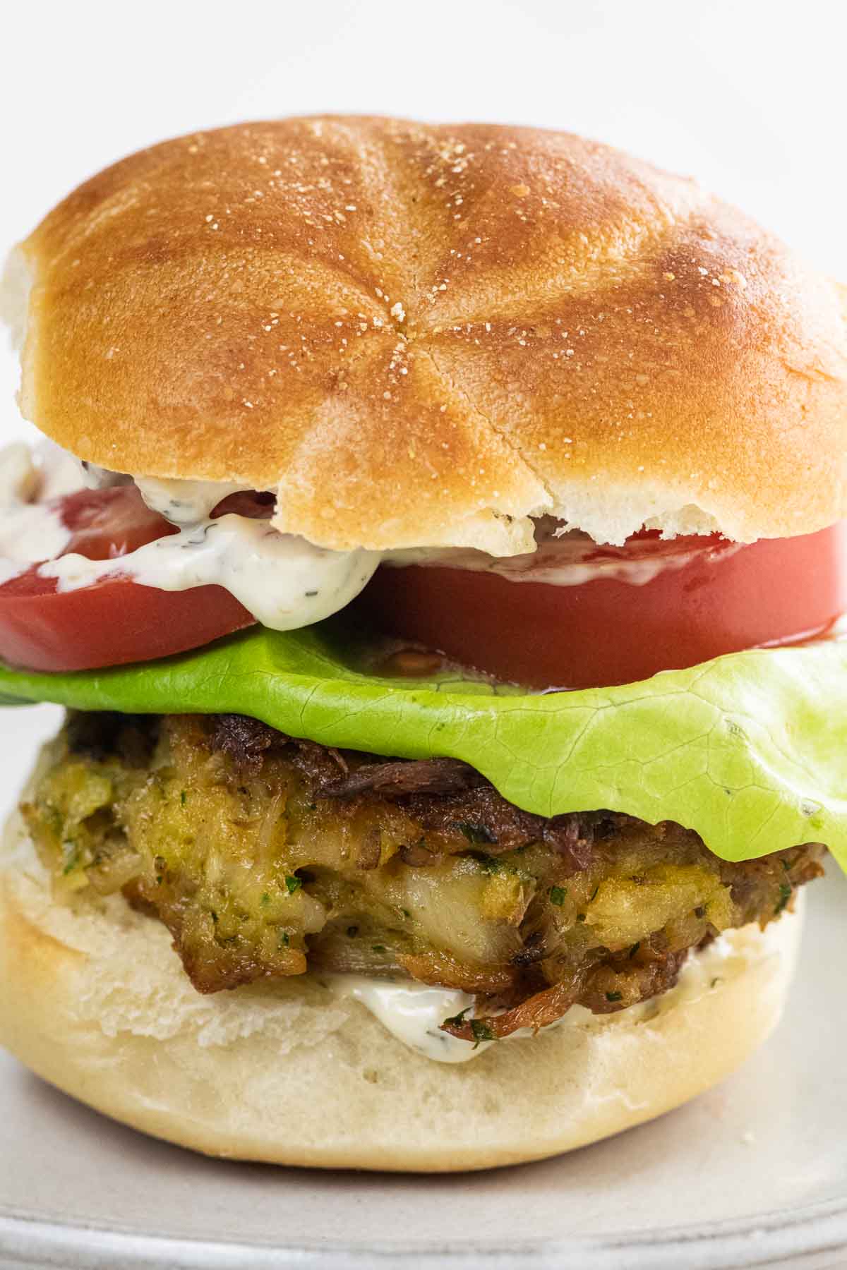 a crab cake sandwich on a kaiser roll with lettuce, tomato, and tartar sauce