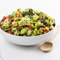 black bean corn avocado salad with jicama in a white bowl with a wooden spoon