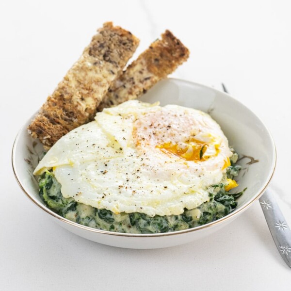 a fried egg over creamed spinach with toast soldiers in a shallow bowl with a fork