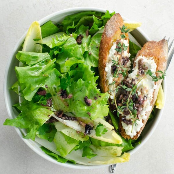 endive and escarole salad with goat cheese croutons and anchovy olive vinaigrette in a bowl with a fork