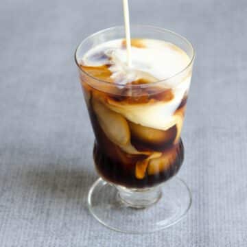 french press cold brew in a glass with ice and milk being poured in