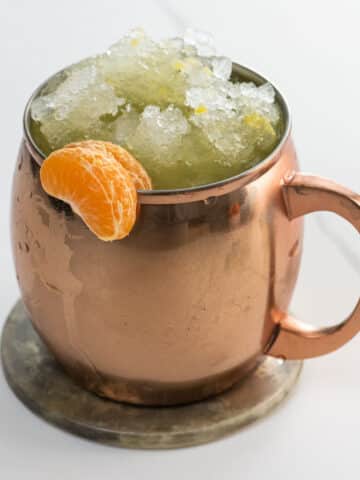 an orange moscow mule in a copper mug garnished with clementine segments
