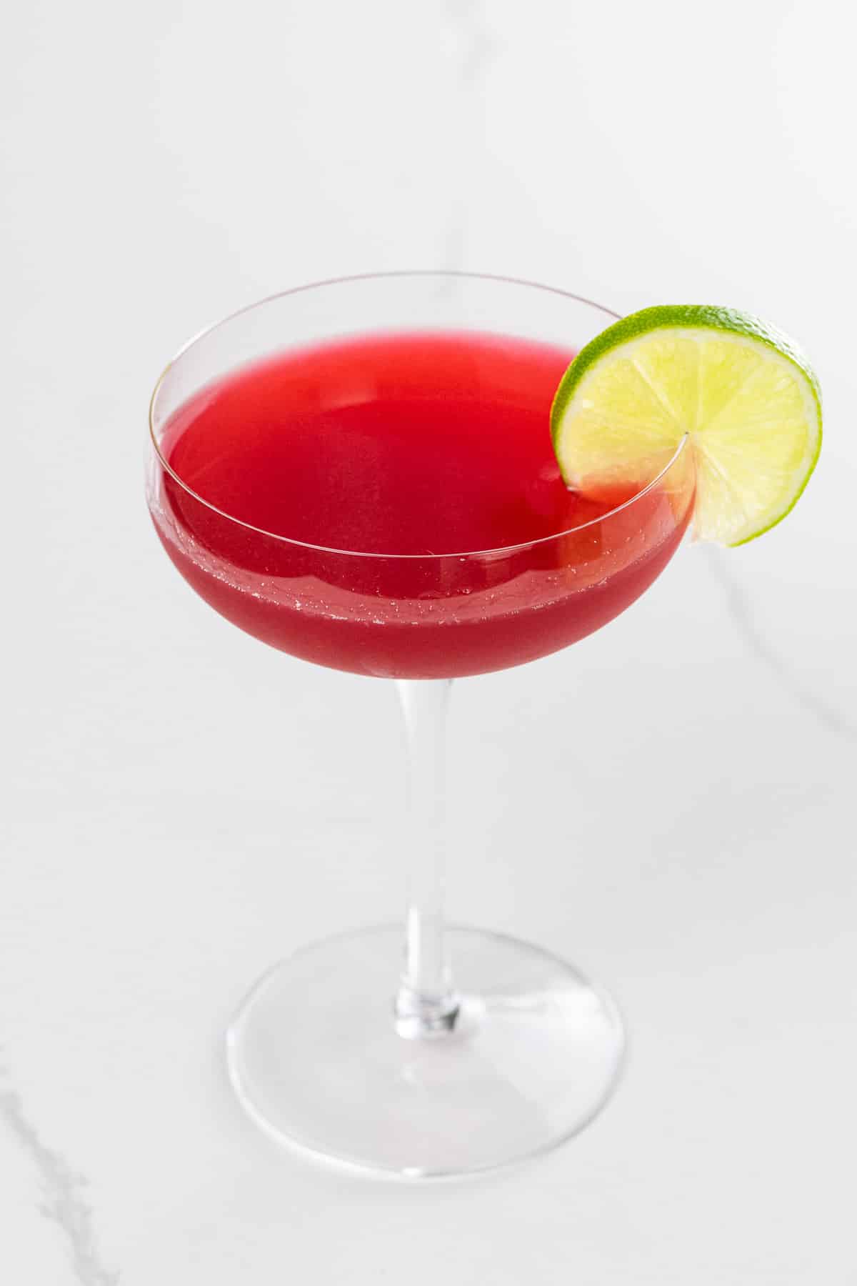 a raspberry gimlet in a coupe glass garnished with a lime wheel