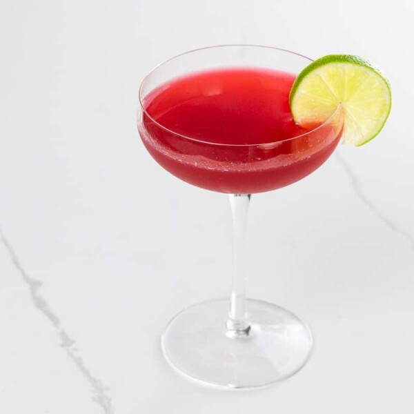 a raspberry gimlet in a coupe glass garnished with a lime wheel