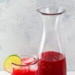raspberry limeade in a carafe and in a glass garnished with a lime wheel