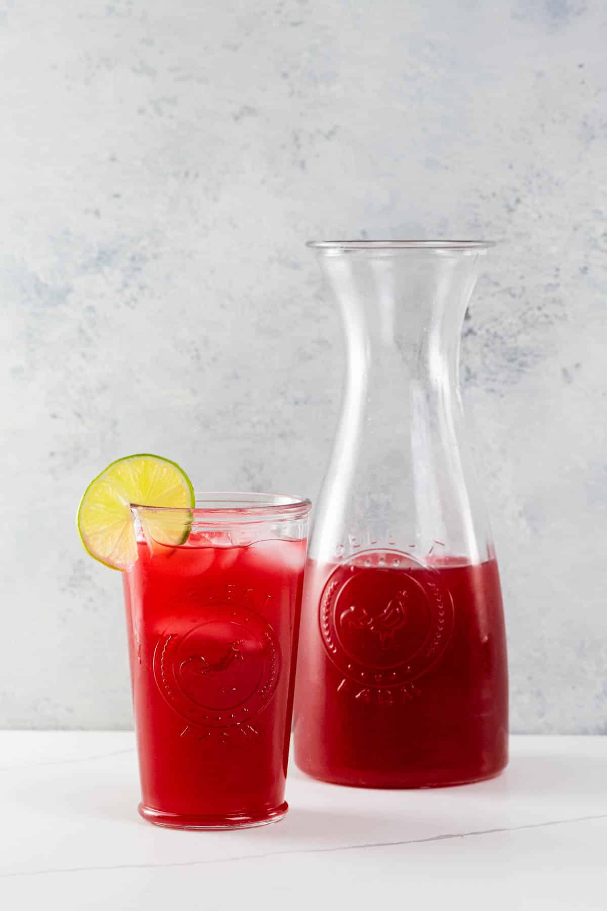 raspberry limeade in a carafe and in a glass garnished with a lime wheel